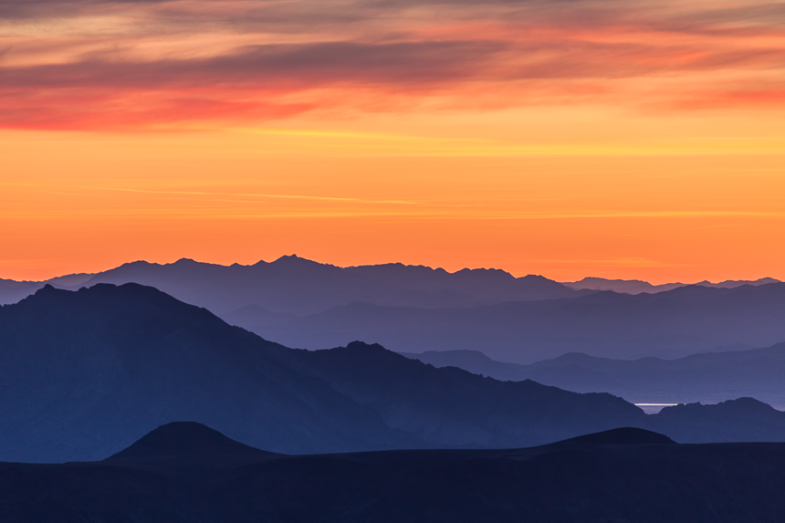 photograph at sunrise with an orange sky and layers of purple mountains in the distance, death valley national park