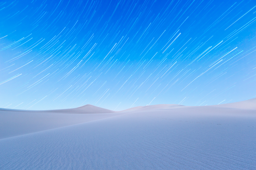 a photograph of the night sky showing star trails over the mesquite sand dunes of death valley national park