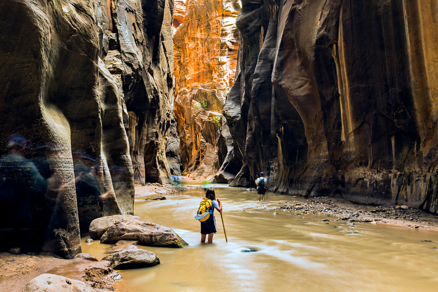 a girl with a walking stick hiking the virgin river narrows in zion national park