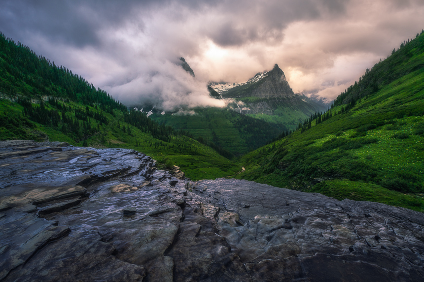 a photograph of mountains in the clouds with bird woman falls in glacier national park montana